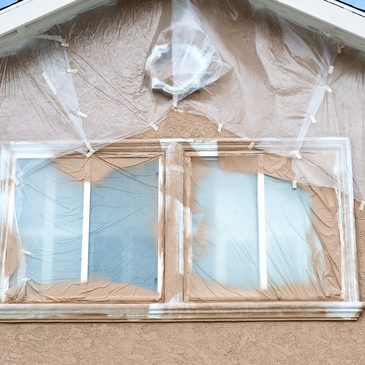 A home is being repainted and is painstakenly masked with plastic sheeting to protect areas from paint overspray during a remodeling project.